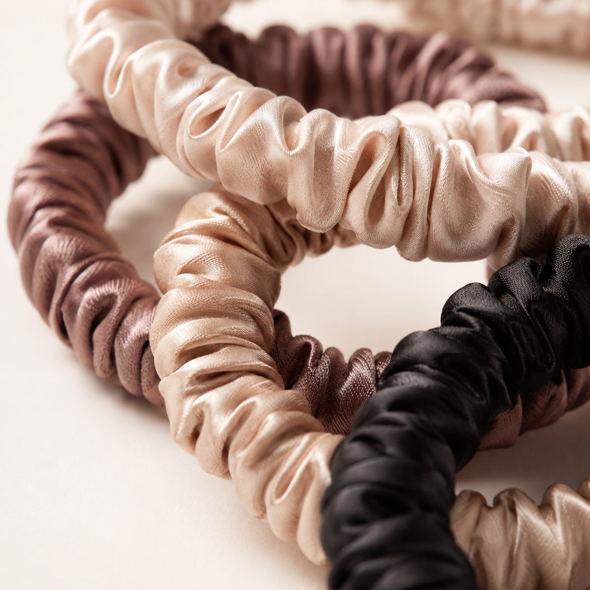 Set of four skinny Silk Scrunchies in cream, champagne, mauve brown and black, showing the gathered silk
